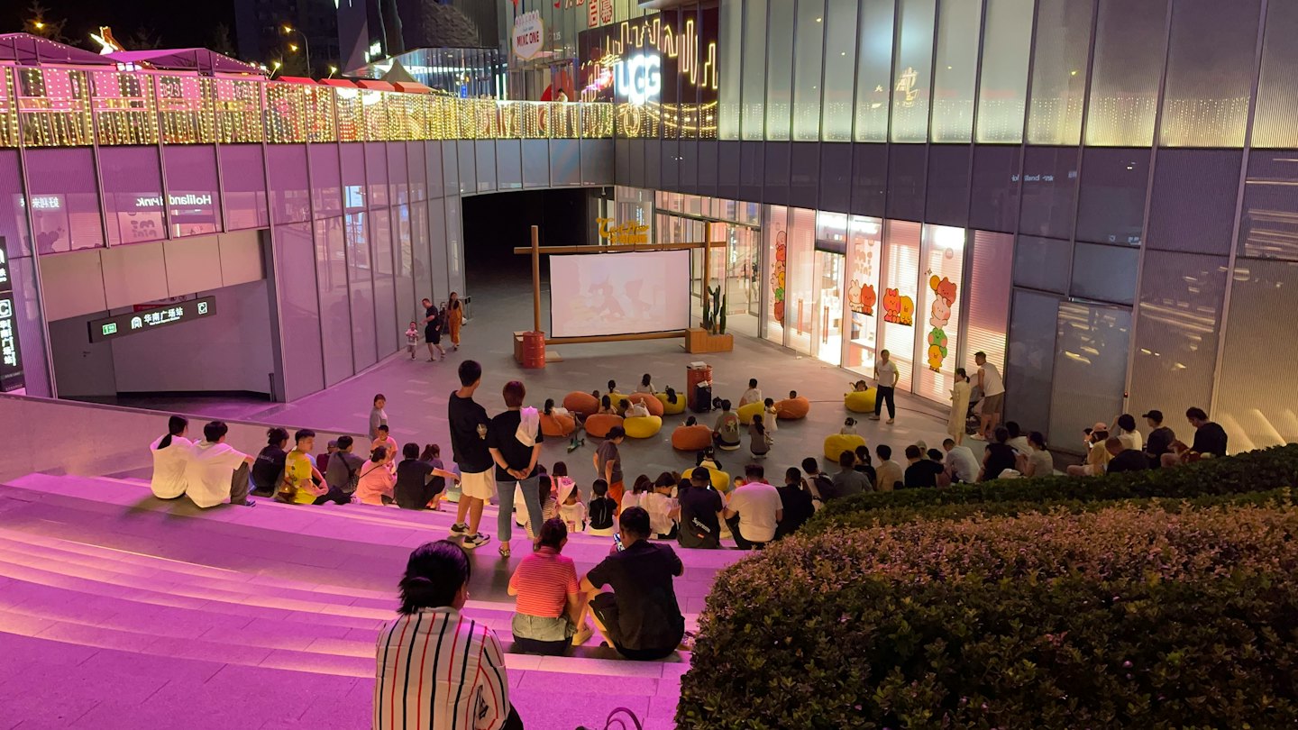 People watch an outdoor movie on a modern city plaza.