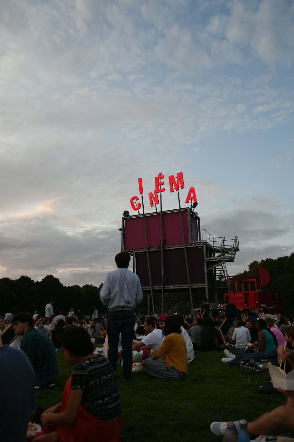 People gather on a grassy field to watch an outdoor cinema.