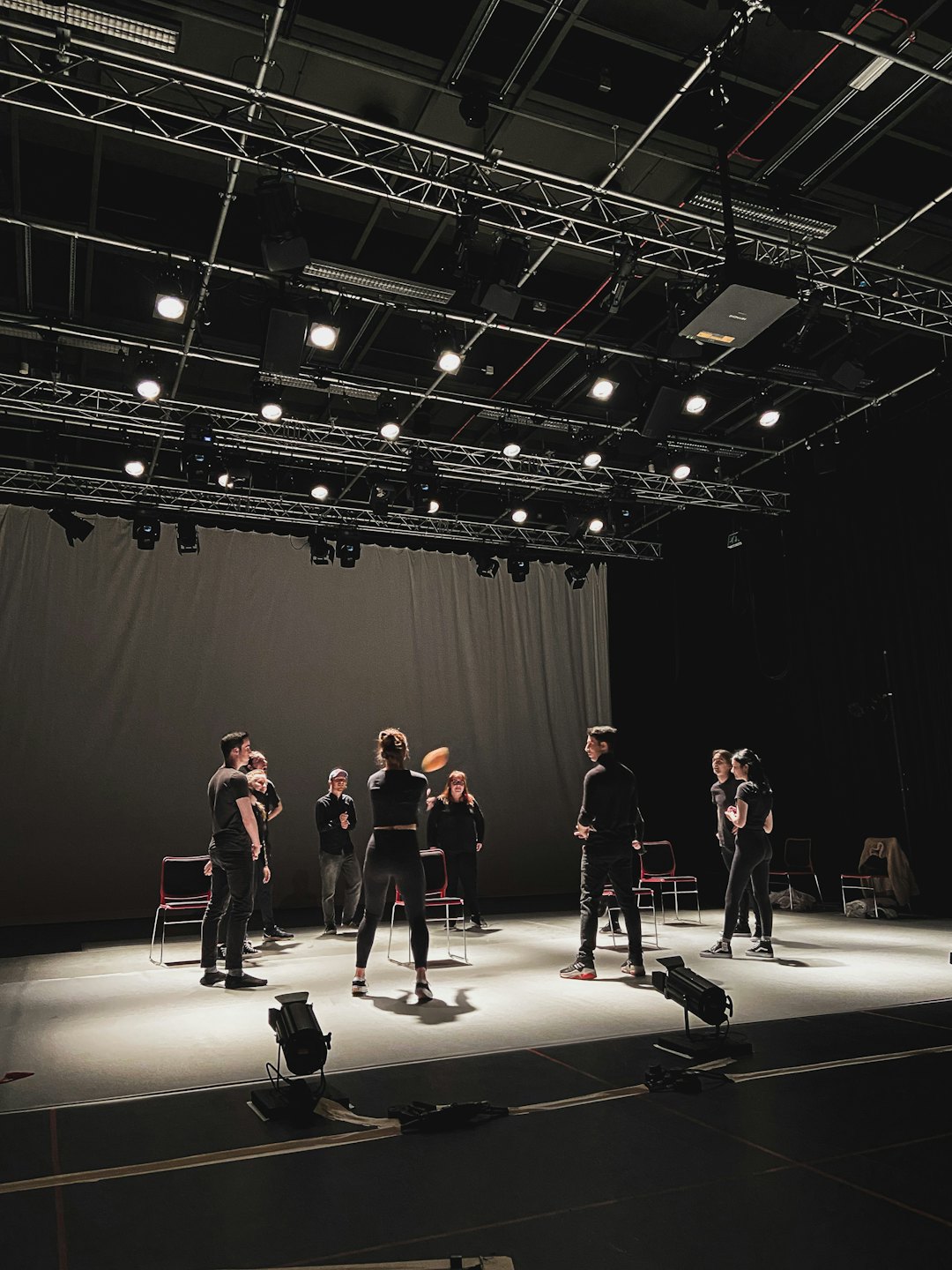 Young adults rehearse on a dimly lit stage with spotlights.