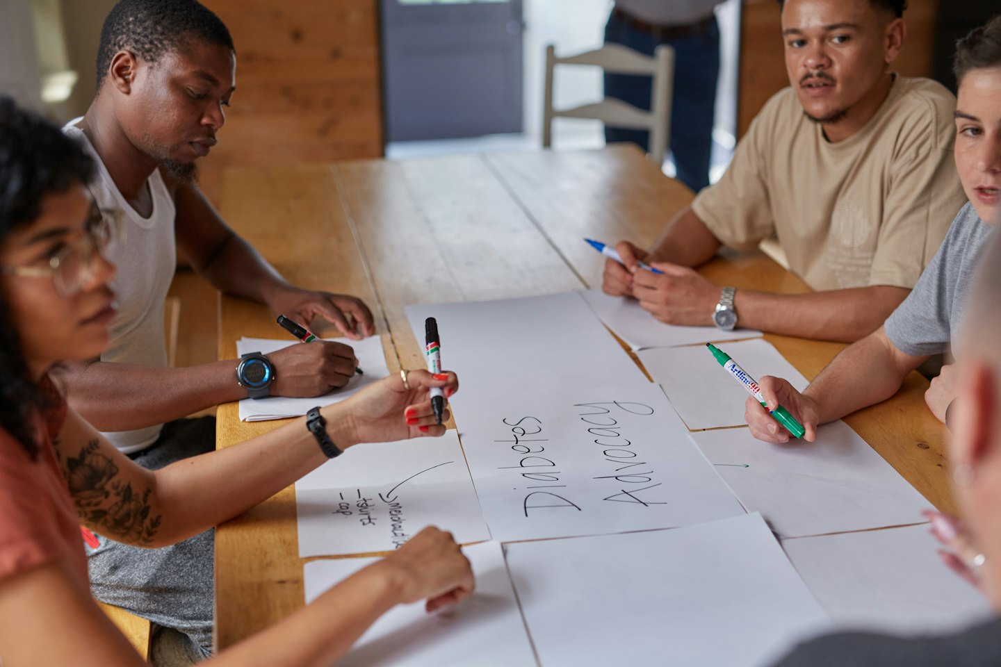 Diverse young adults brainstorm ideas around a table.